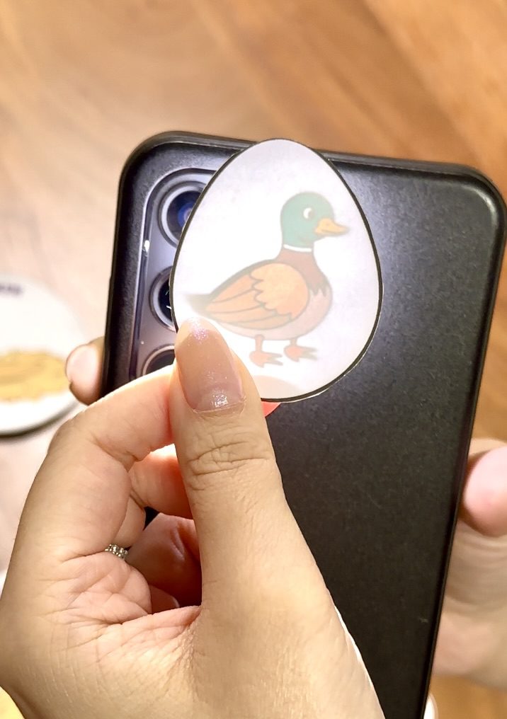 Phone flashlight shining through paper egg revealing a duck inside